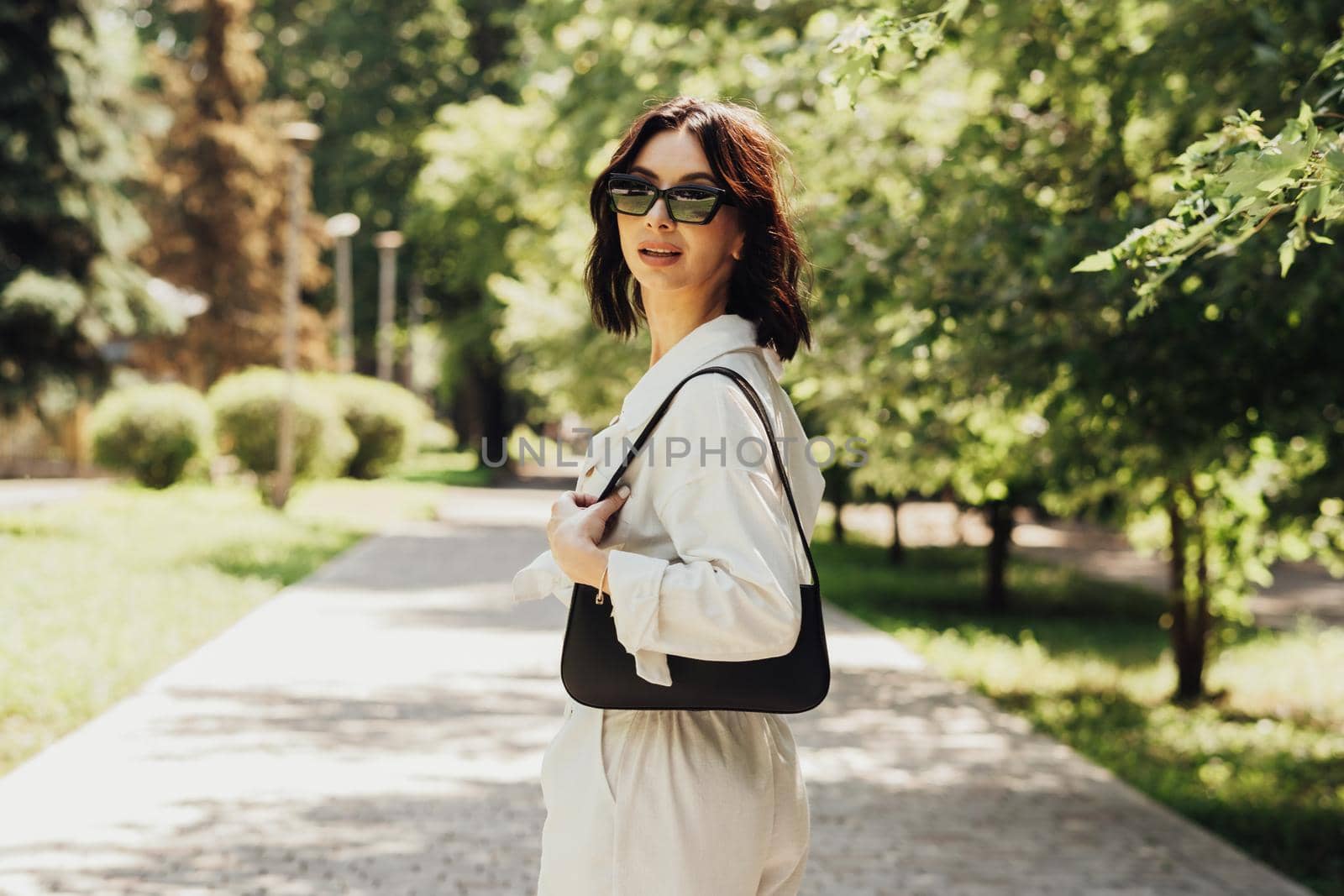 Portrait of Stylish Brunette Woman in Sunglasses with Hand Bag Outdoors at Sunny Summer Day
