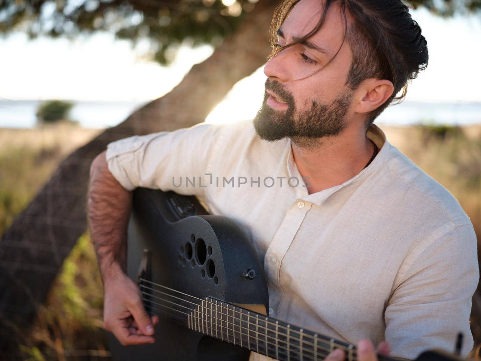Guitarist in a shirt singing with a grey guitar in the countryside, horizontal close up