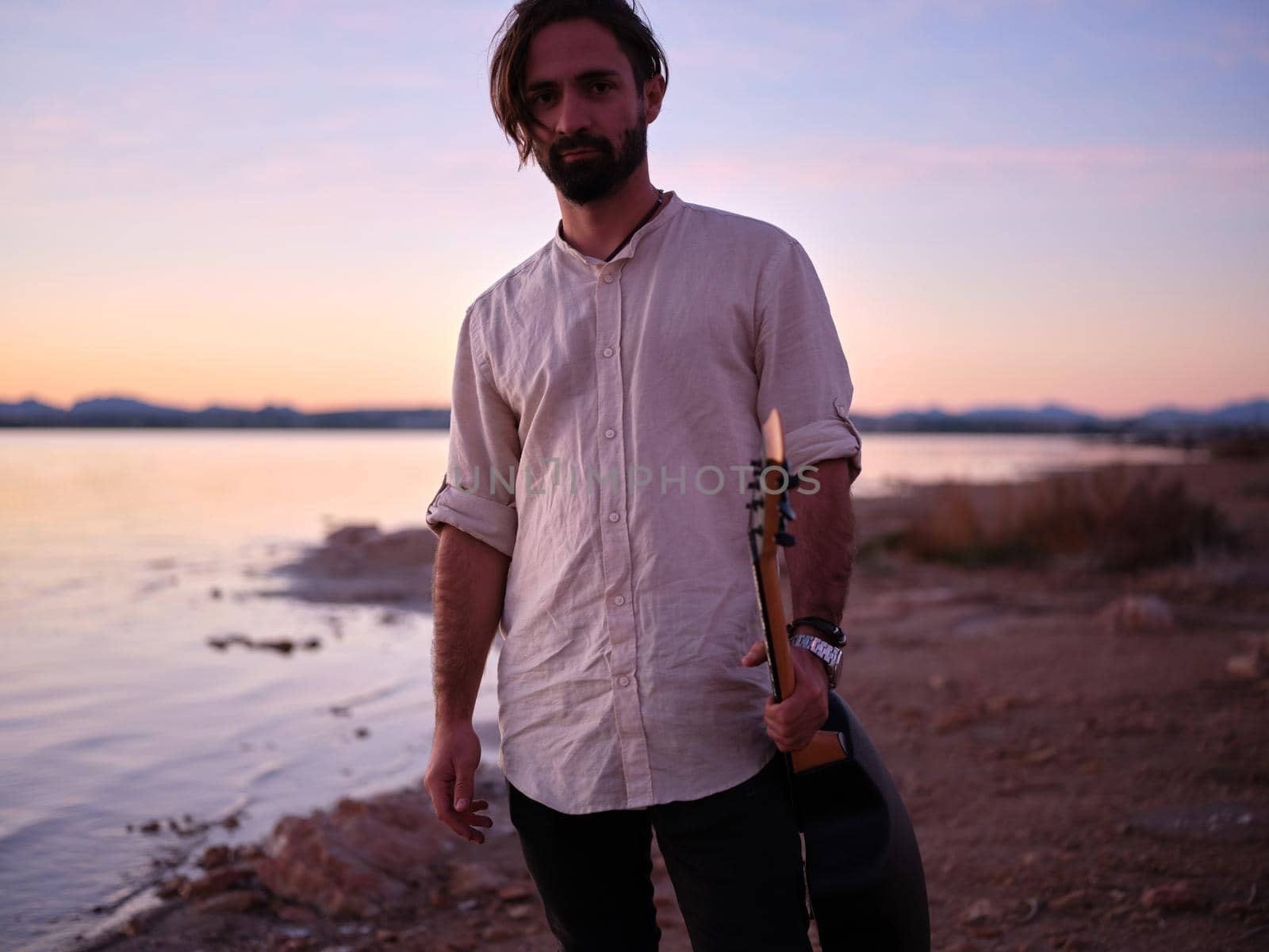 guitarist posing with his guitar next to the pink lake, horizontal portrait during dusk