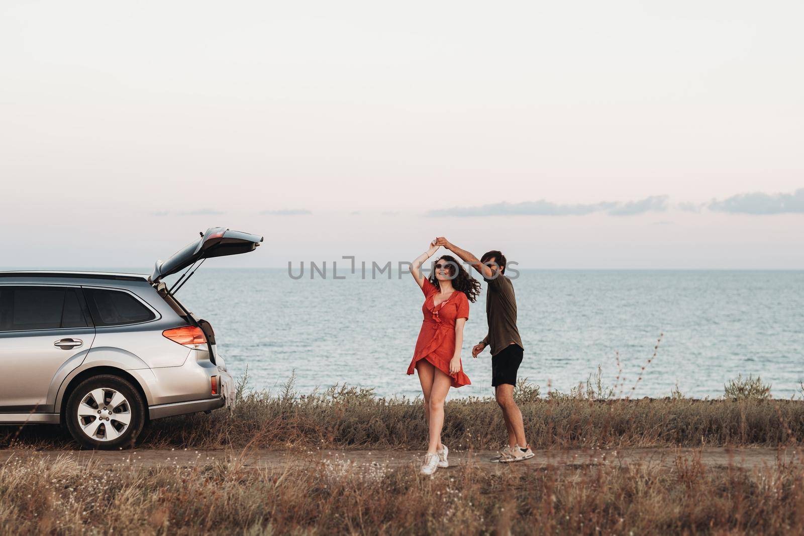 Youth Couple Having Fun on the Background of Sea, Man and Woman Dancing Near Their SUV Car at Sunset