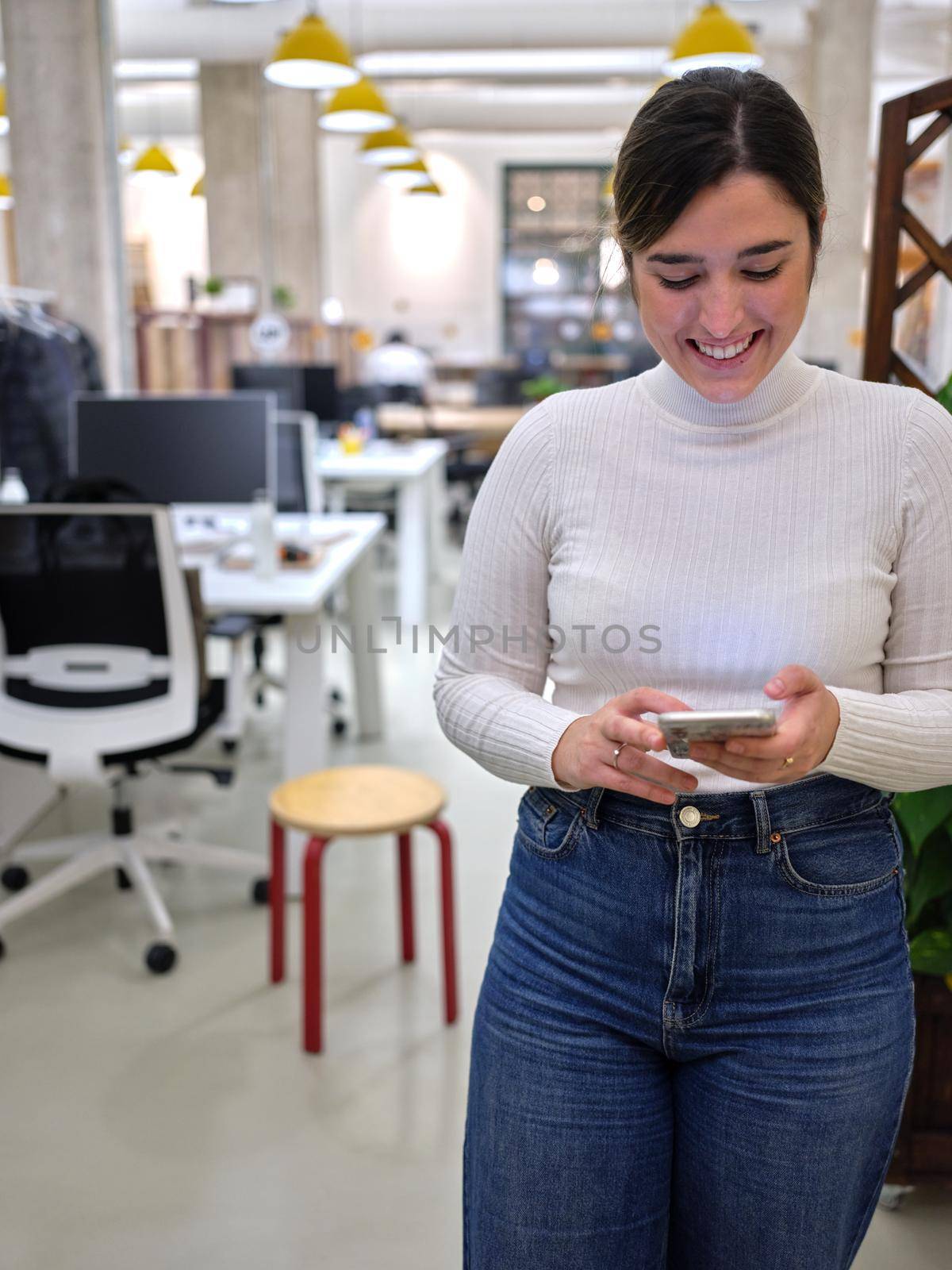 woman standing smiling looking at her mobile phone in the office, vertical background