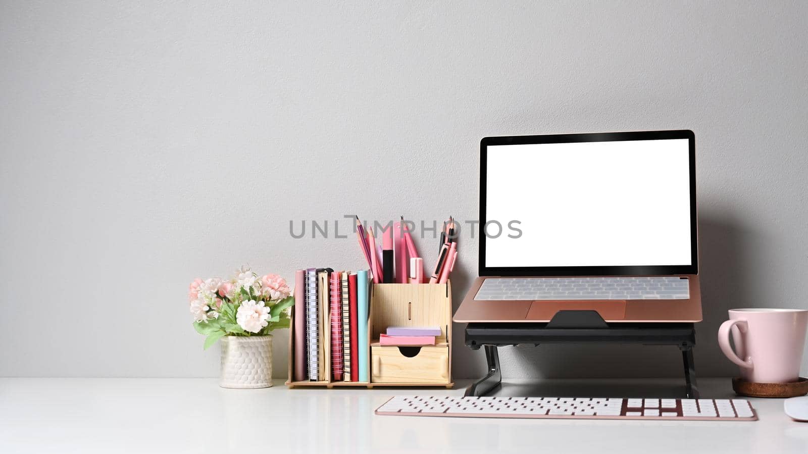 Home office desk with computer laptop, flower pot and coffee cup on white table.