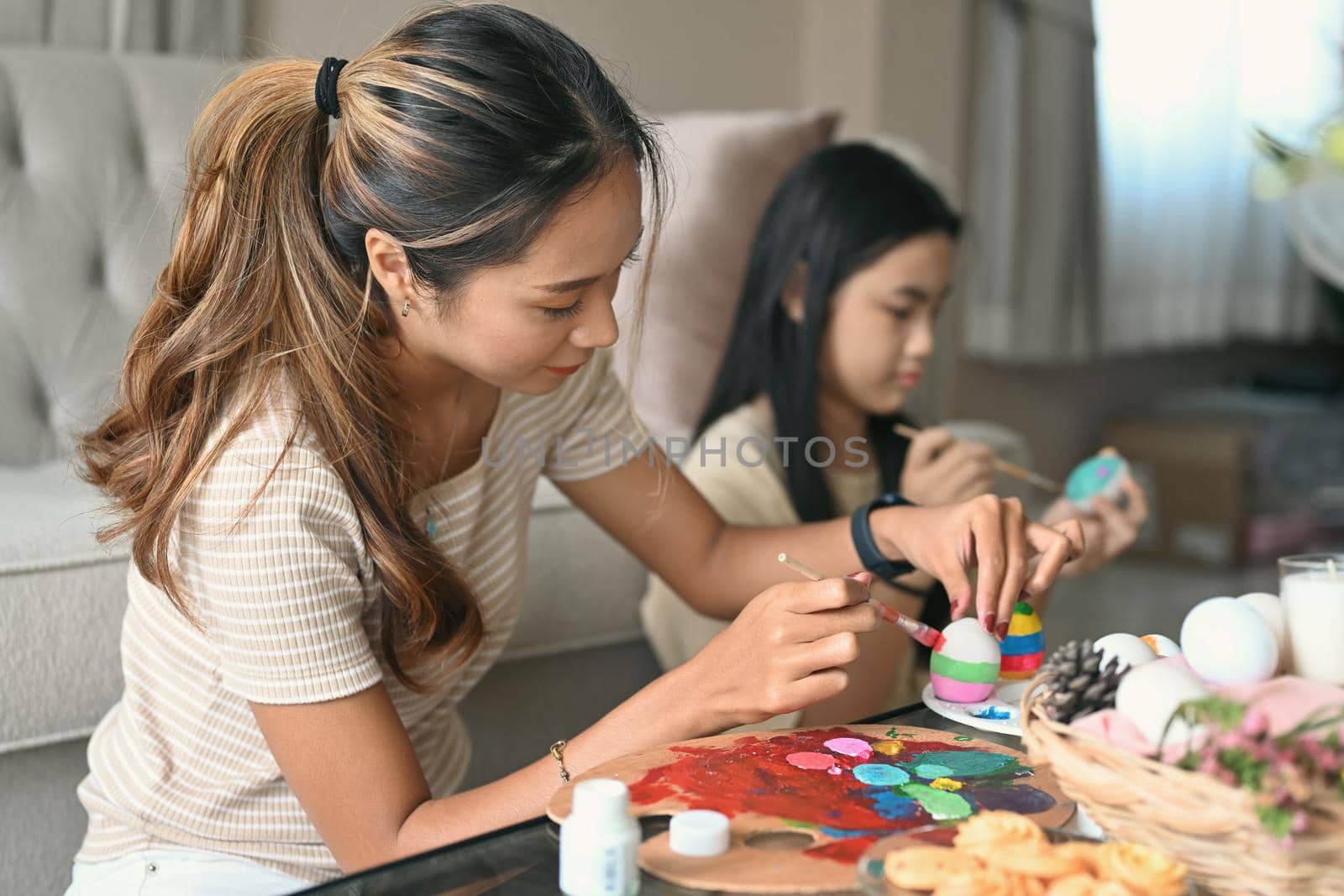 Asian mother and daughter painting Easter eggs together at home. by prathanchorruangsak