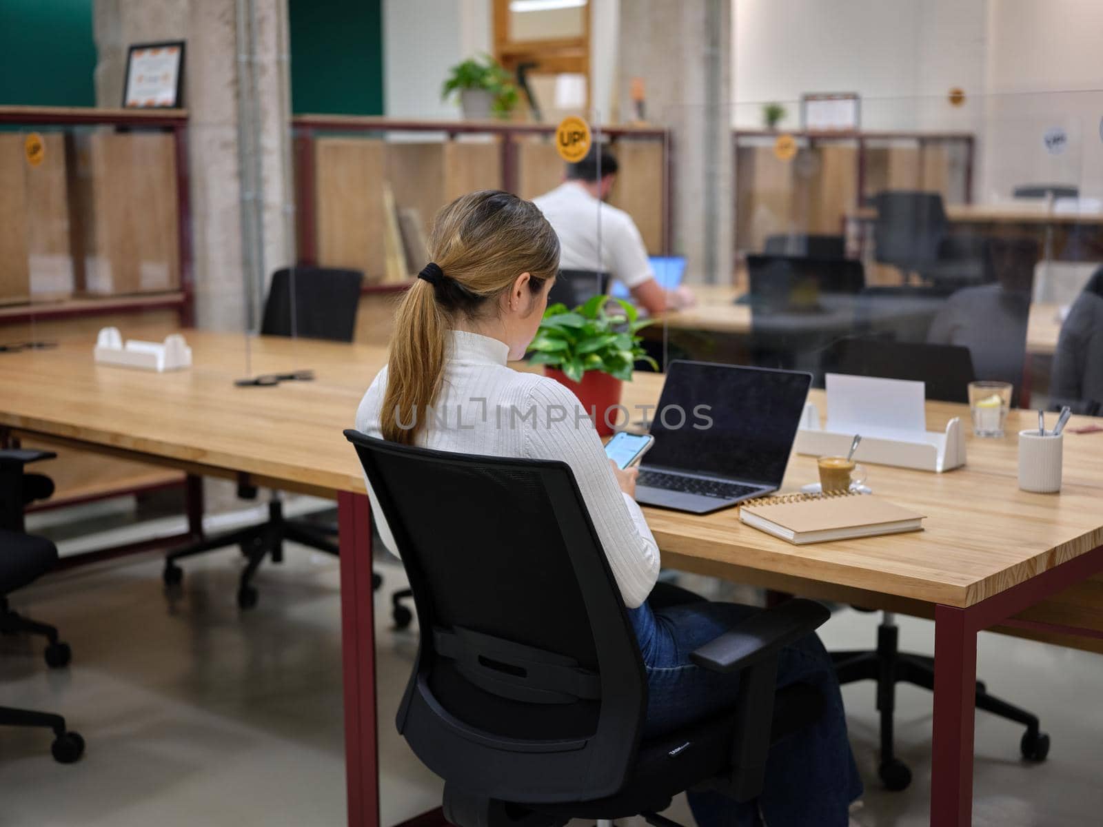 woman with her mobile phone sitting in a coworking space with other people by WesternExoticStockers