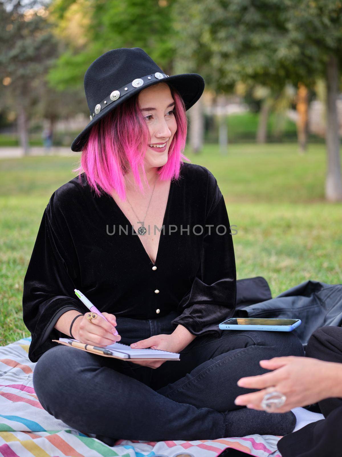 smiling girl with pink hair and hat sitting in the park writing in her notebook by WesternExoticStockers