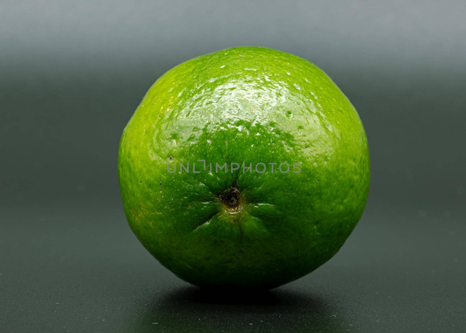 Green lime citruss fruit peel textured with black dots, macro photo, black background