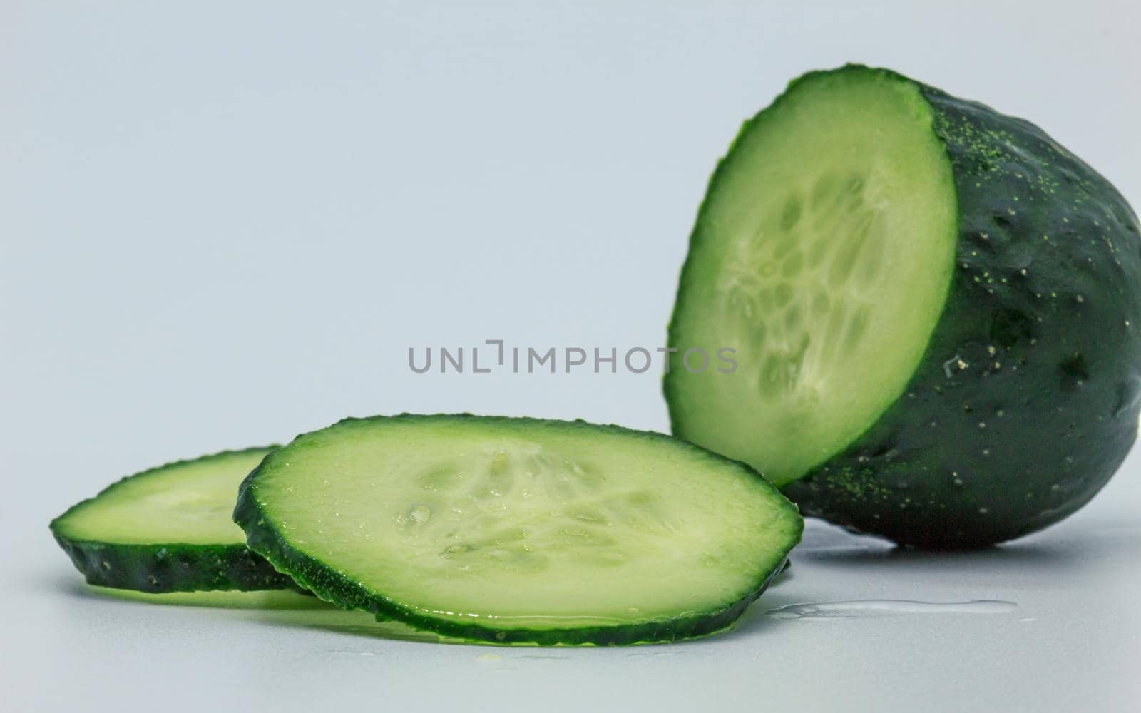 Green wet cucumber half piece of vegetable and two cutted pieces, inside macro view, white background