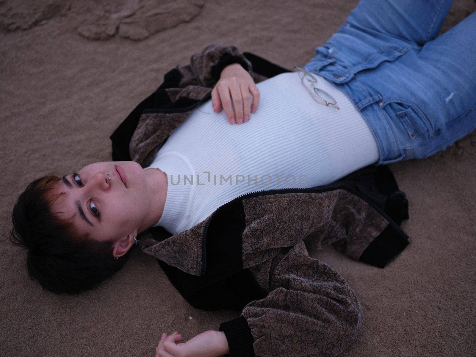 non-binary girl posing lying on the sand on the beach and looking at the camera, horizontal cutout