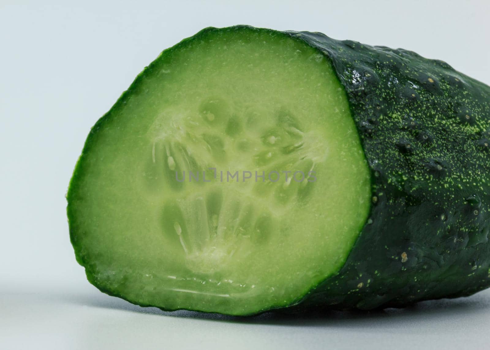 Green wet cucumber half piece of vegetable, inside macro view, white background