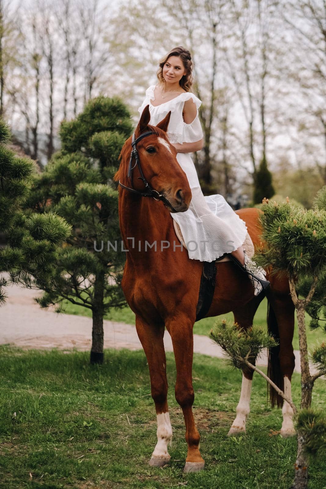 A woman in a white sundress riding a horse near a farm.
