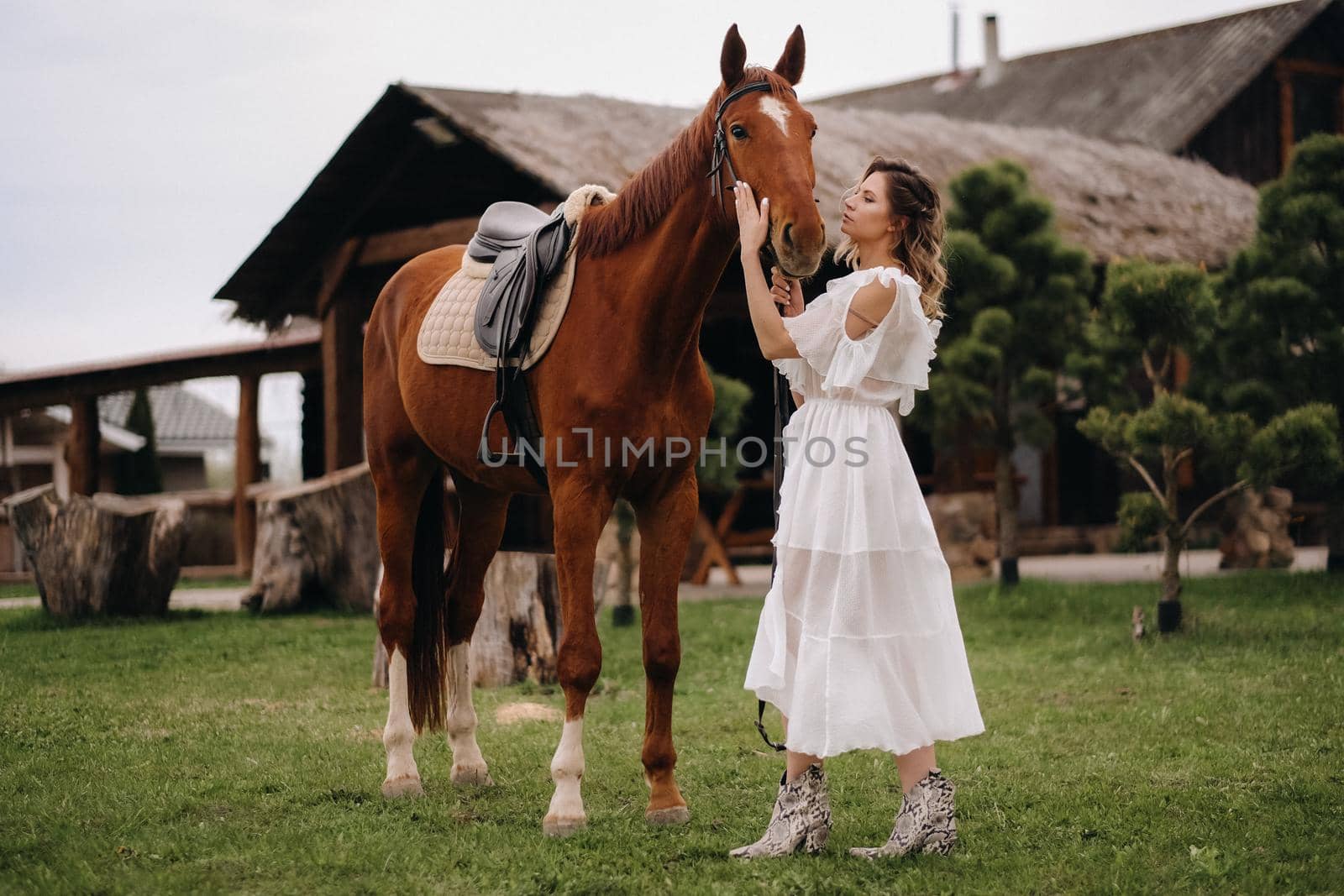 Beautiful girl in a white sundress next to a horse on an old ranch.