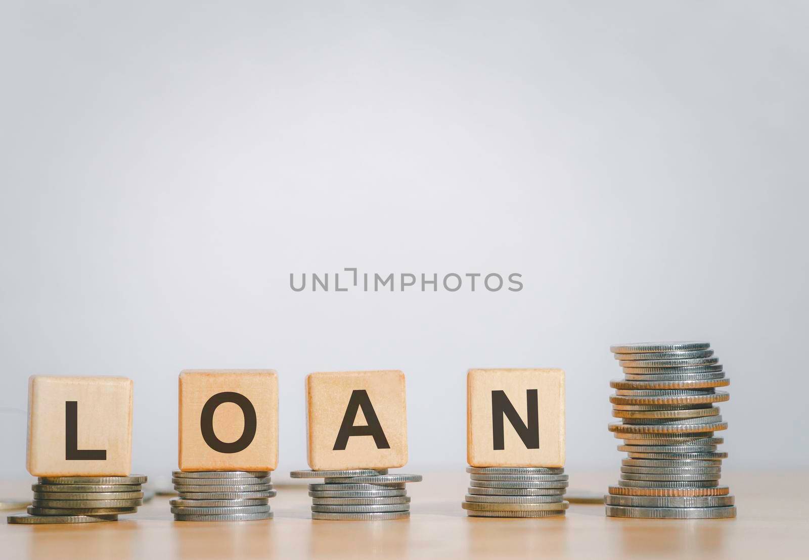 Close Up wooden block written LOAN against on stack coins to business and finance concept. Fees and Interest from loans are main revenue for banks. Loans can be unsecured such as credit card.