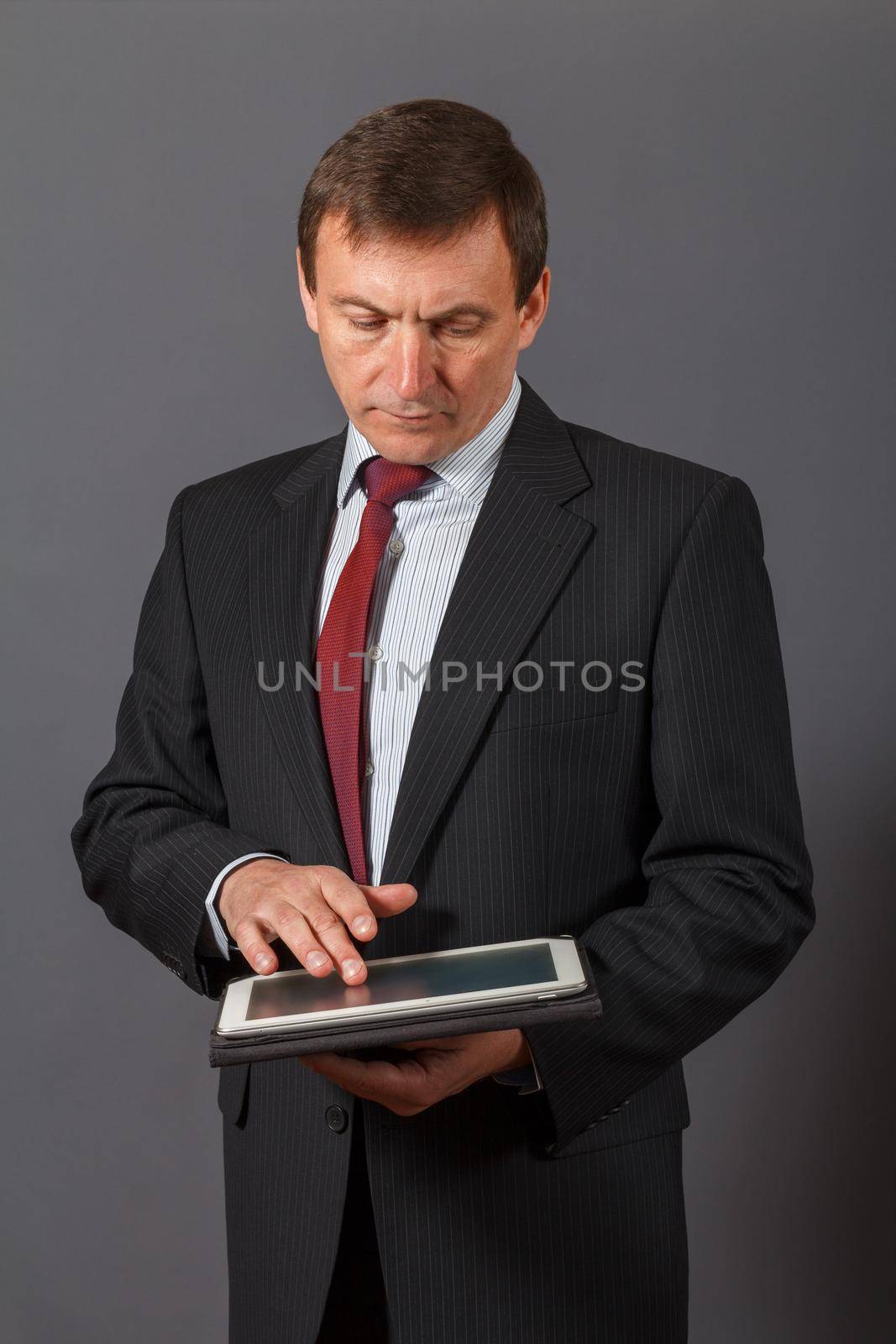 Confident and friendly elegant handsome mature businessman standing in front of a grey background holding a notebook