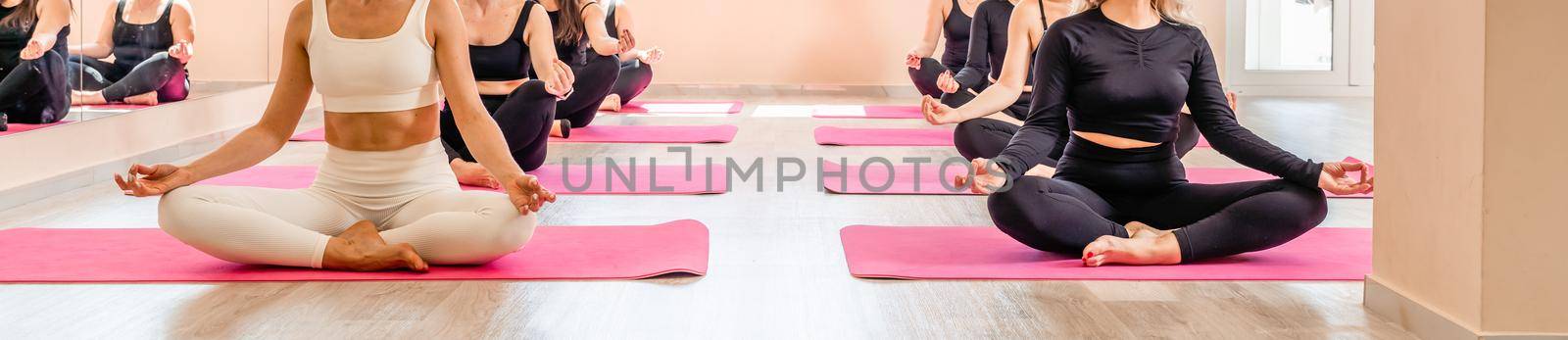 A group of sportswomen doing pilates or yoga on pink mats in a beige loft studio interior. Teamwork, good mood and healthy lifestyle concept