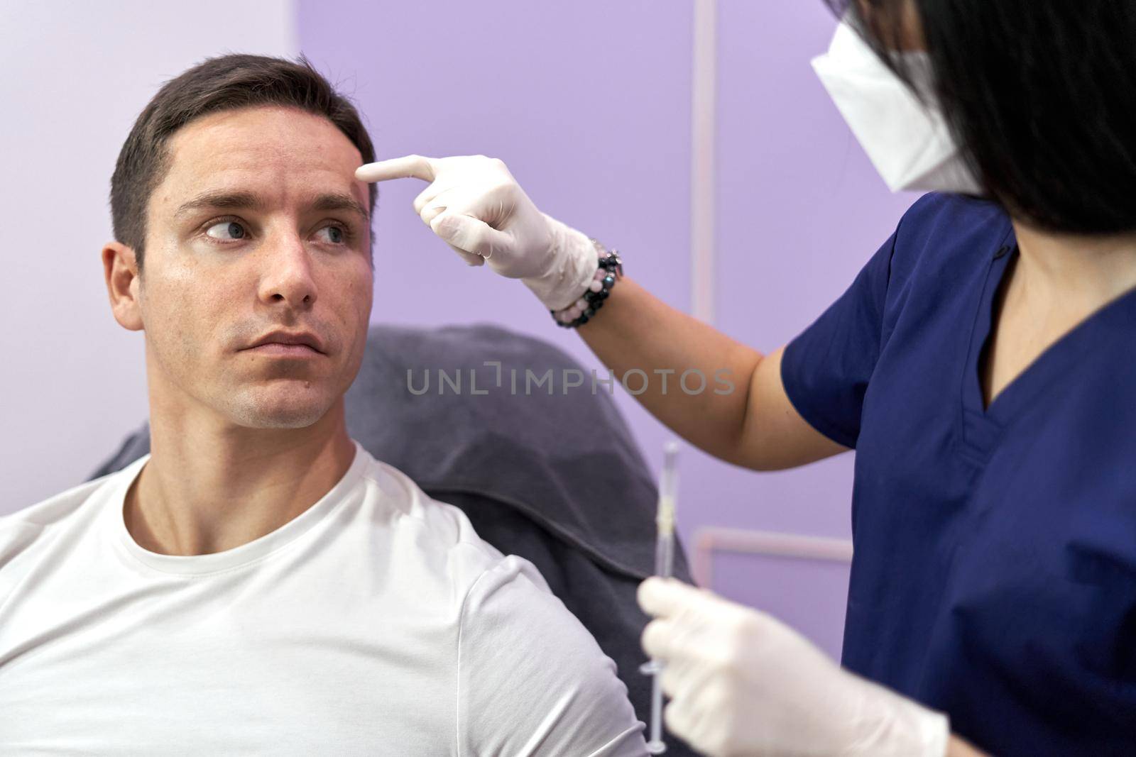 Doctor pointing to the spot where she will inject a botox injection to a man for a beauty treatment