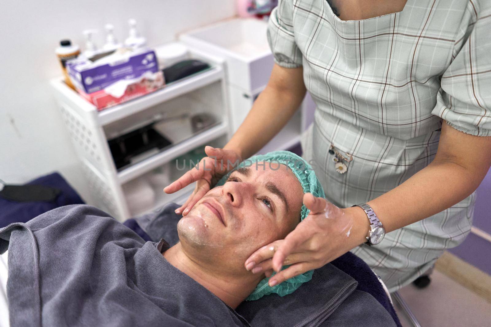 A nurse's hands massaging a patient's face before receiving a facial beauty treatment in a clinic