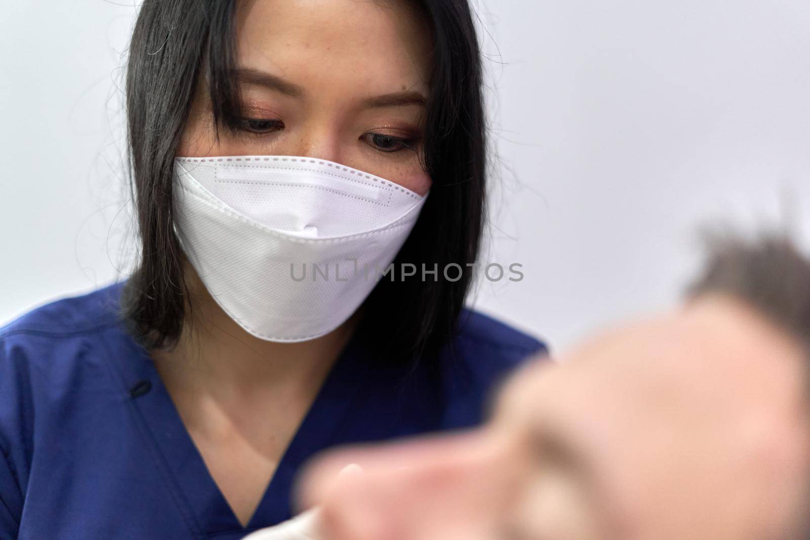 Focus on a female doctor in a mask and uniform concentrating on a patient by WesternExoticStockers