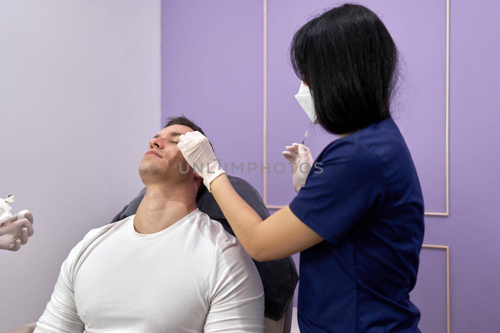 Doctor cleaning the area where she will inject a vaccine of botox for a beauty treatment to a man