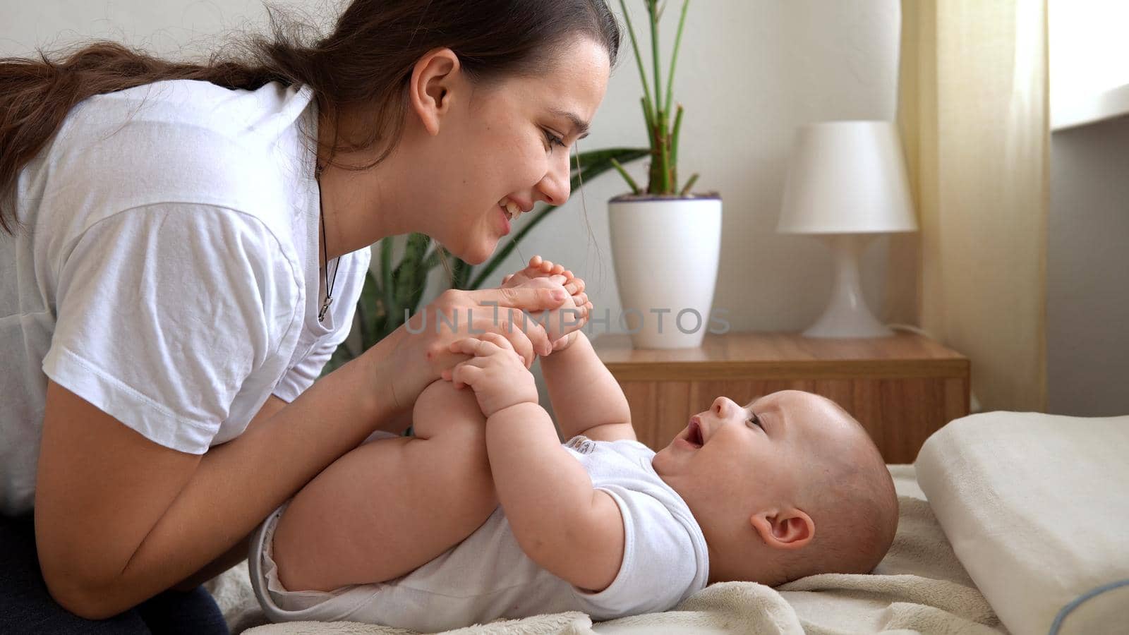 Authentic Young Caucasian Woman Holding Newborn Baby. Mom And Child On Bed. Close-up Portrait of Smiling Family With Infant On Hands. Happy Marriage Couple On Background. Childhood, Parenthood Concept.