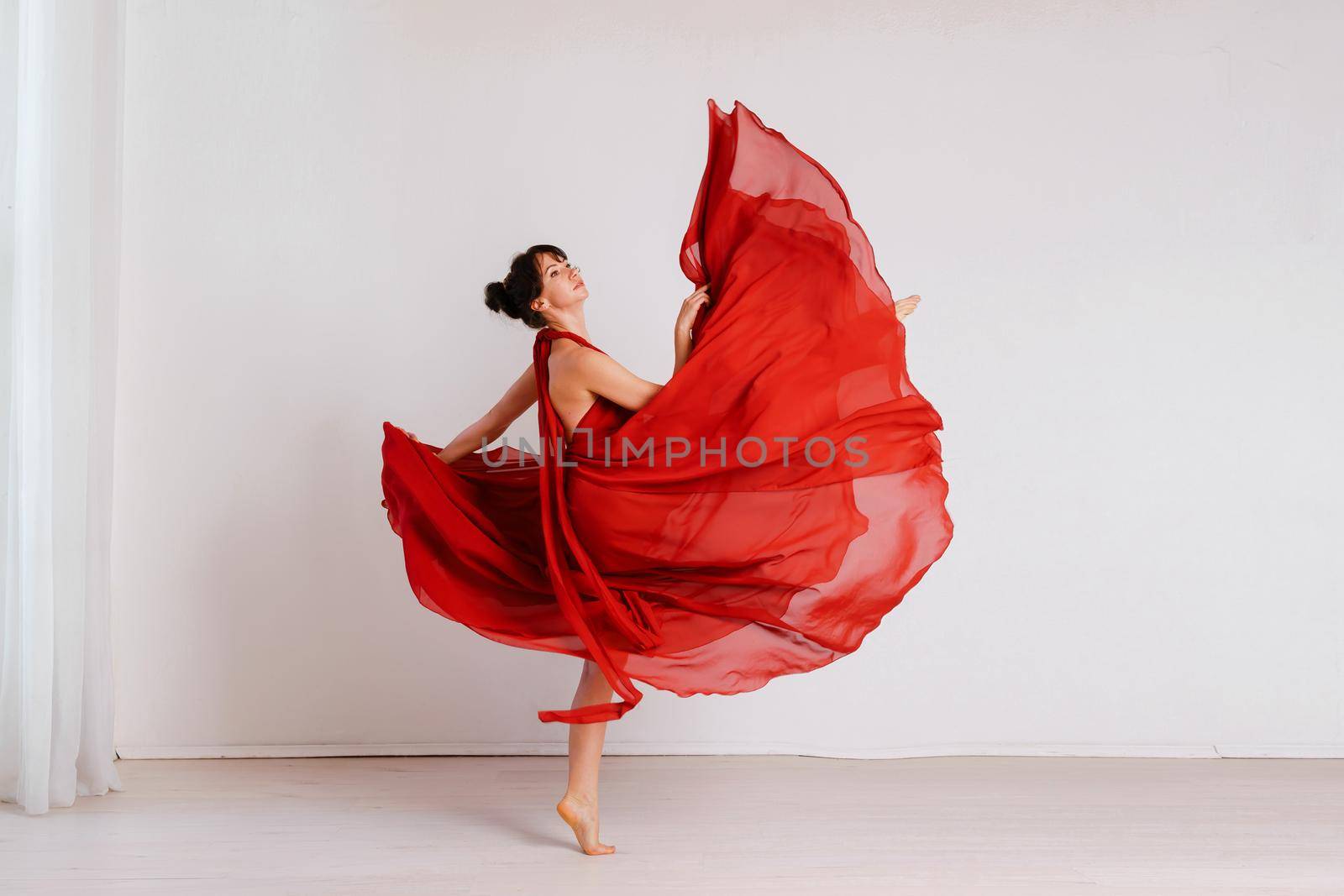 Dancer in a red flying dress. Woman ballerina dancing on a white studio background by Matiunina