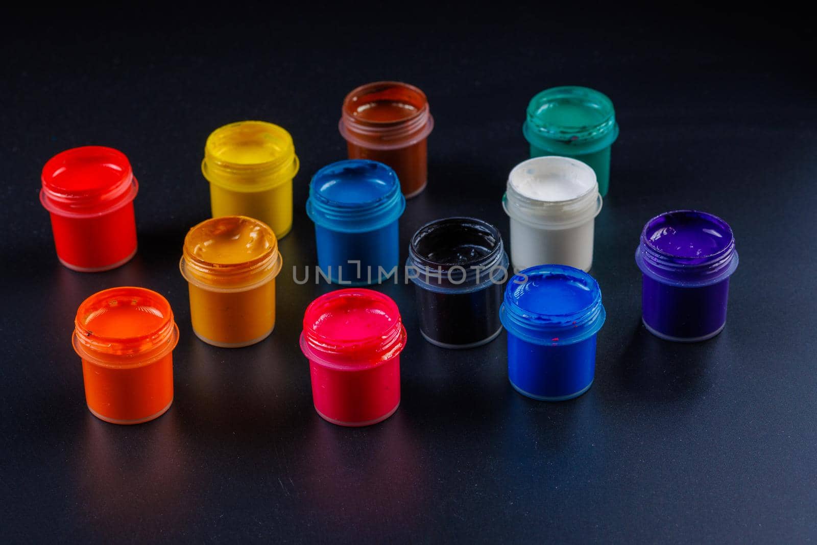 close-up background of opened small gouache paint jars on flat black surface