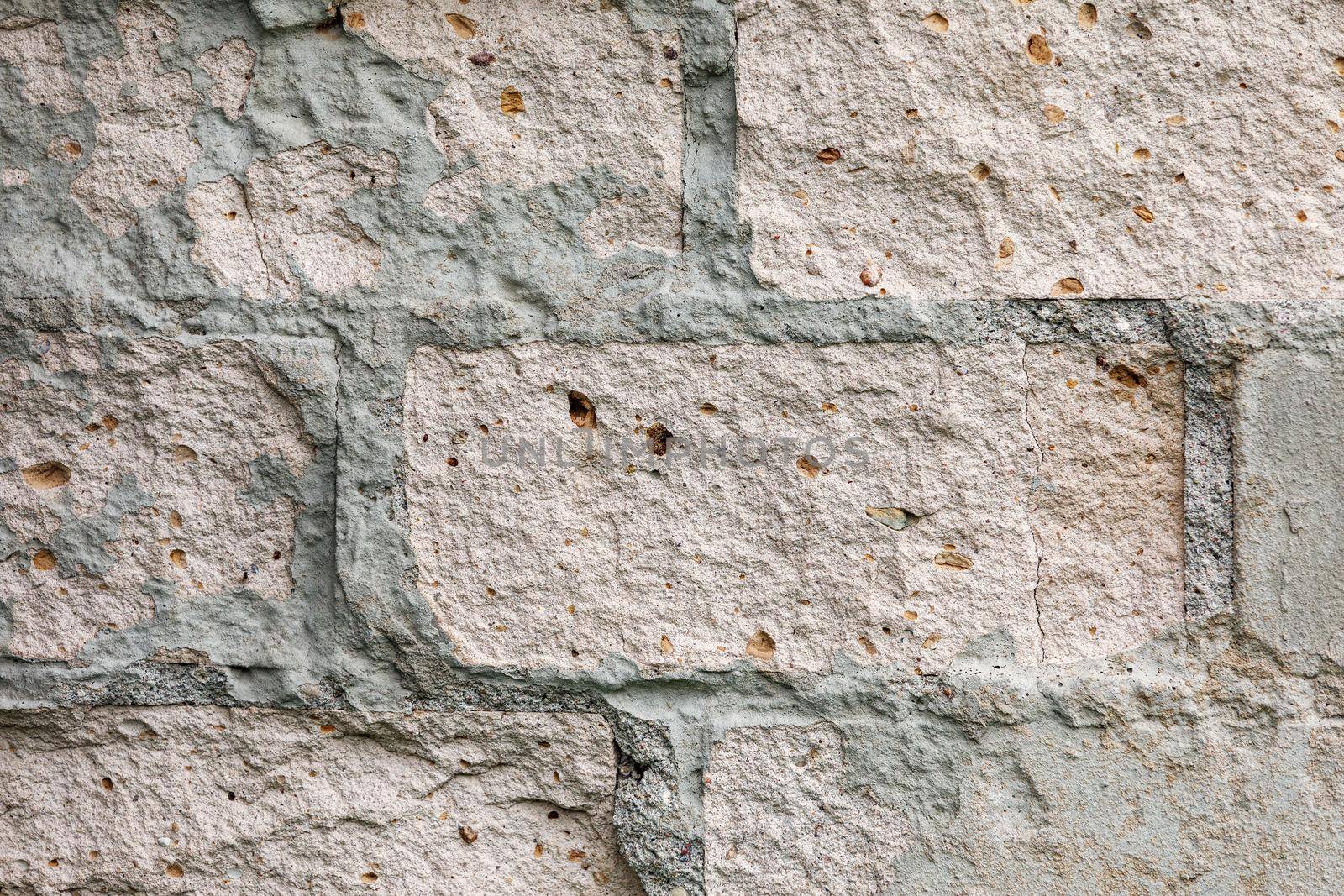 Grey plaster old brick wall with chipped stucco pieces. Grunge white brick wall with damaged surface background