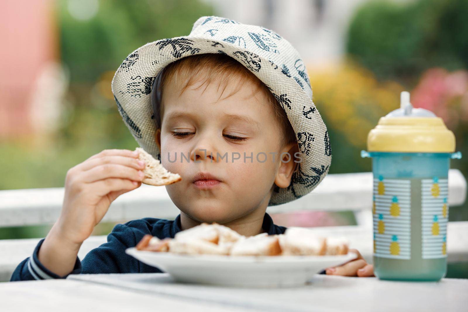 A healthy child eats butter on bread in his grandmother's garden during the summer holidays. A plastic cup with pineapple juice on the table. The concept of healthy food for a child.