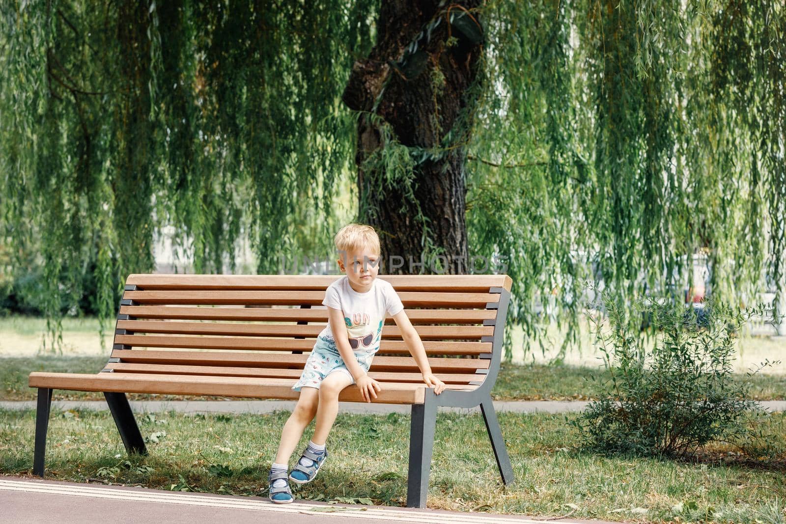 Small child plays in park. Kid is sitting on a park bench. Happy family and childhood concept. Healthy baby outdoors. by Lincikas