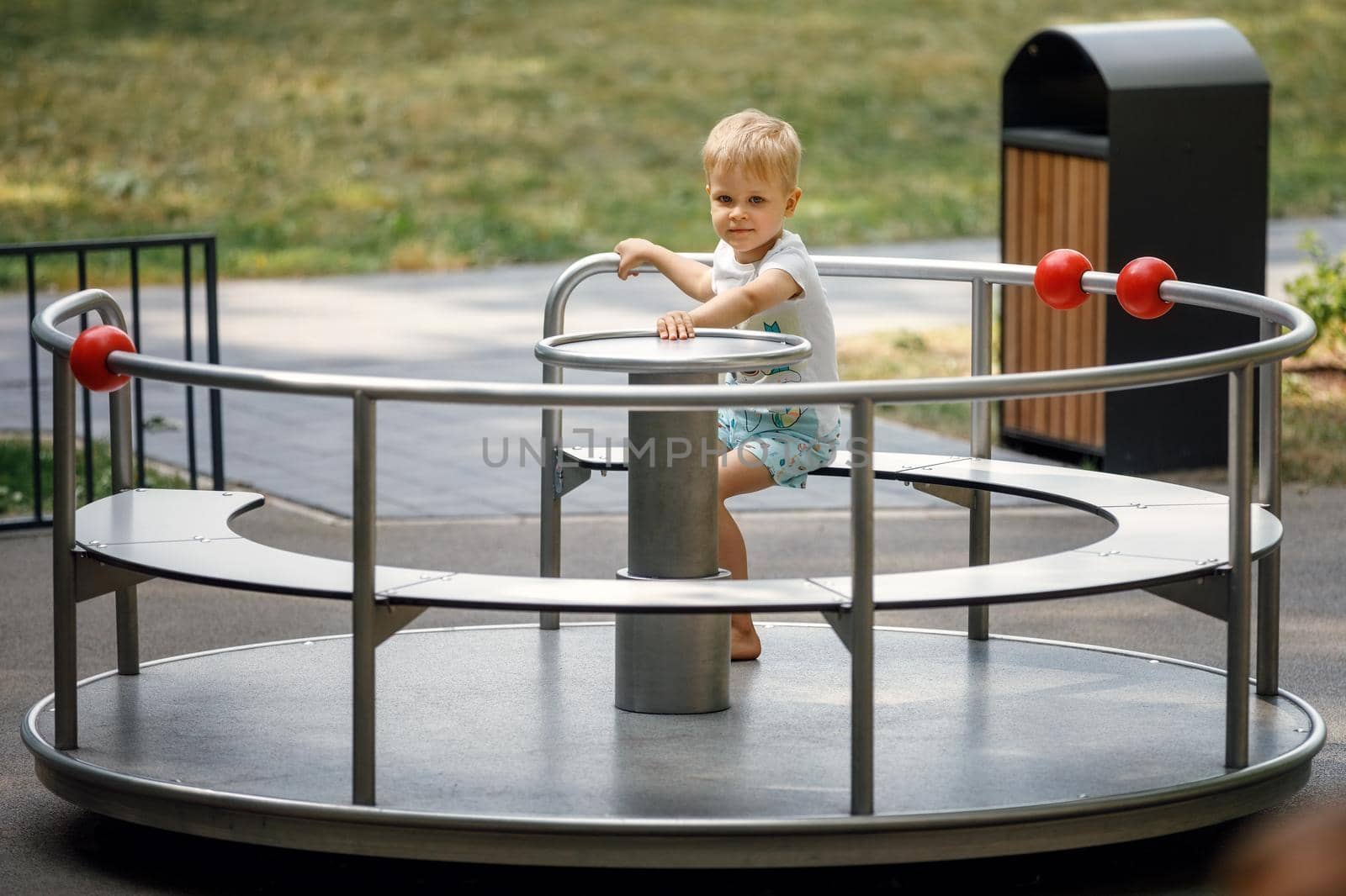 A little boy sits in a metal carousel for children in summer in the park and poses for the camera.