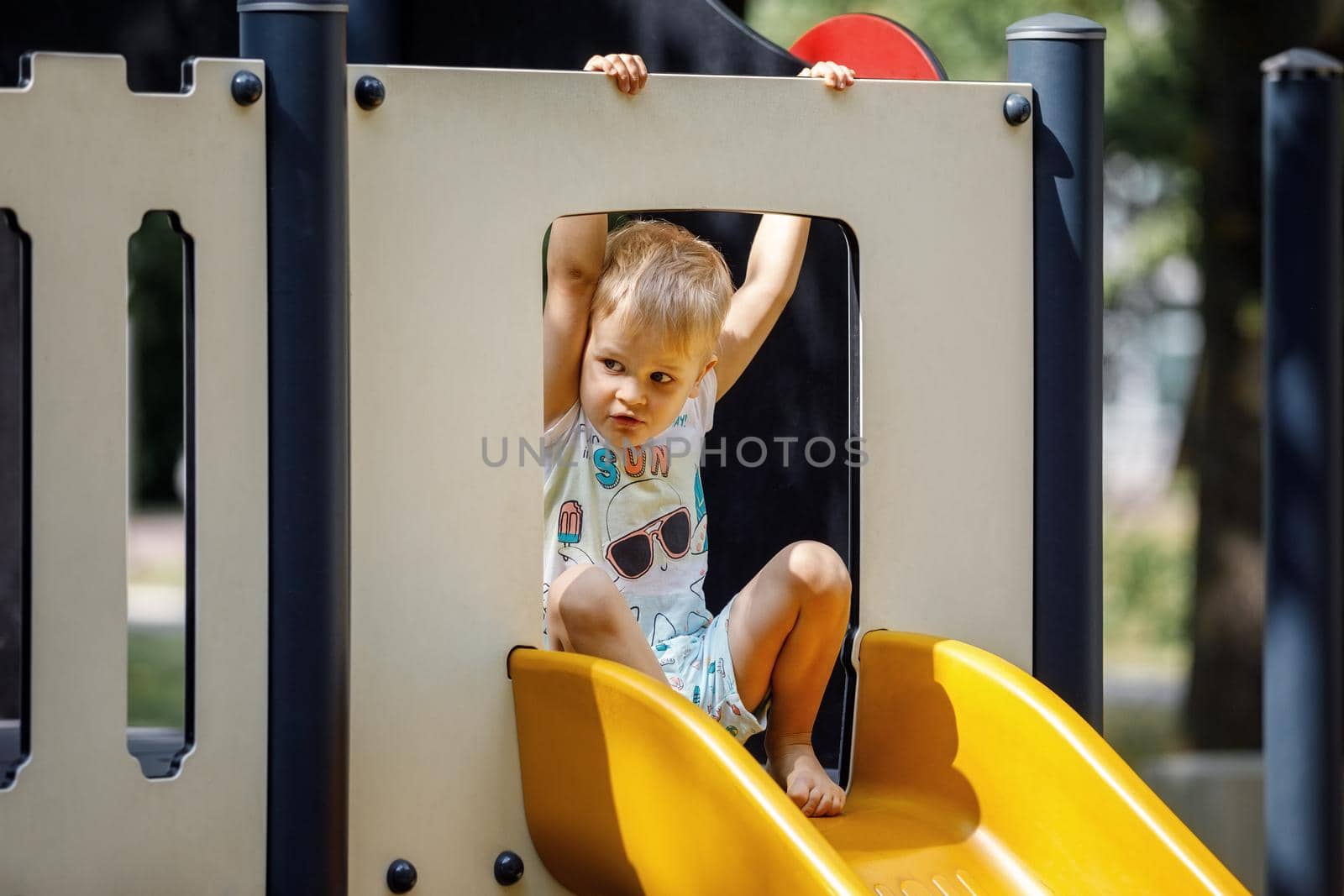 A little boy is ready to slide on a yellow, outdoor playground plastic slide. Horizontal photo.