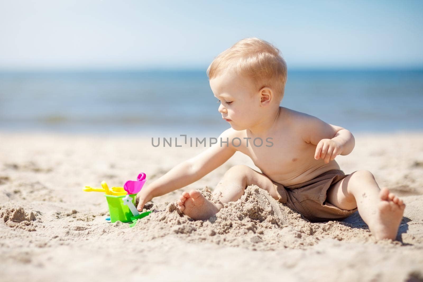 Boy plays in the sand on the beach near the sea. The child is focused and he likes his toys