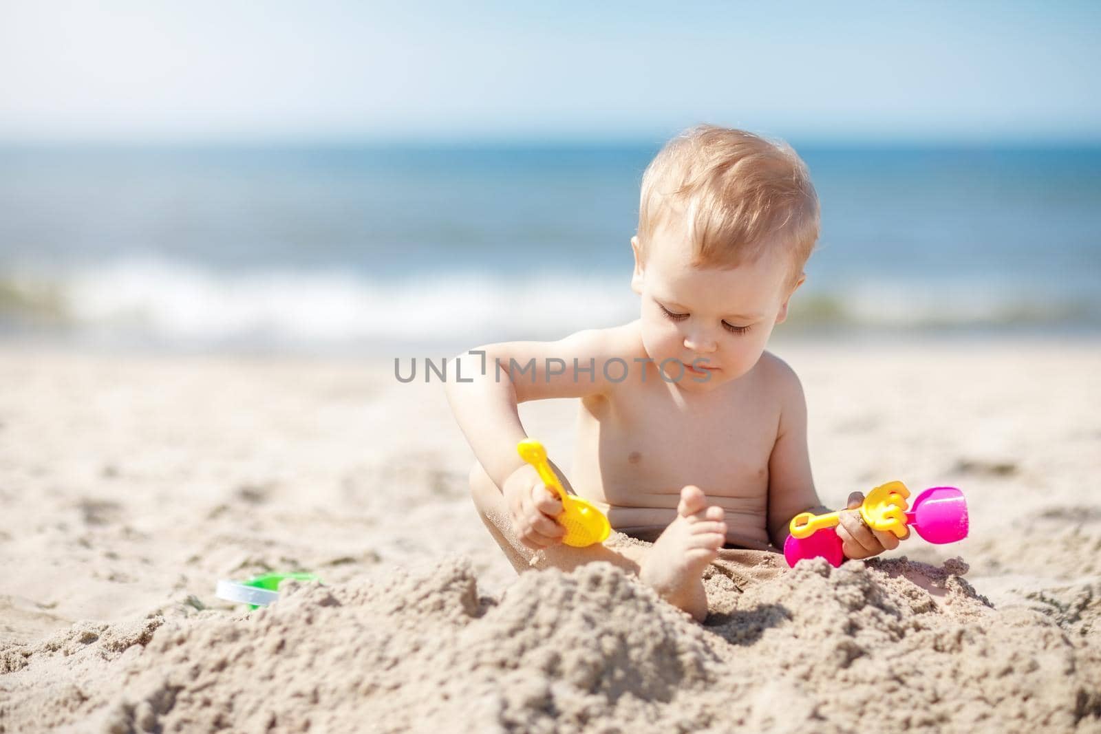 The little boy in the beach, is experimenting with sand trying to pour it on his feet. Holidays by the sea are a great pastime for children.