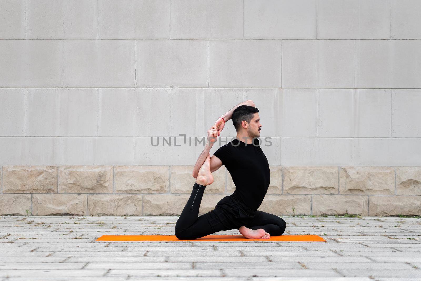 Handsome latin man doing yoga in a city. One Legged King Pigeon Pose. by apavlin