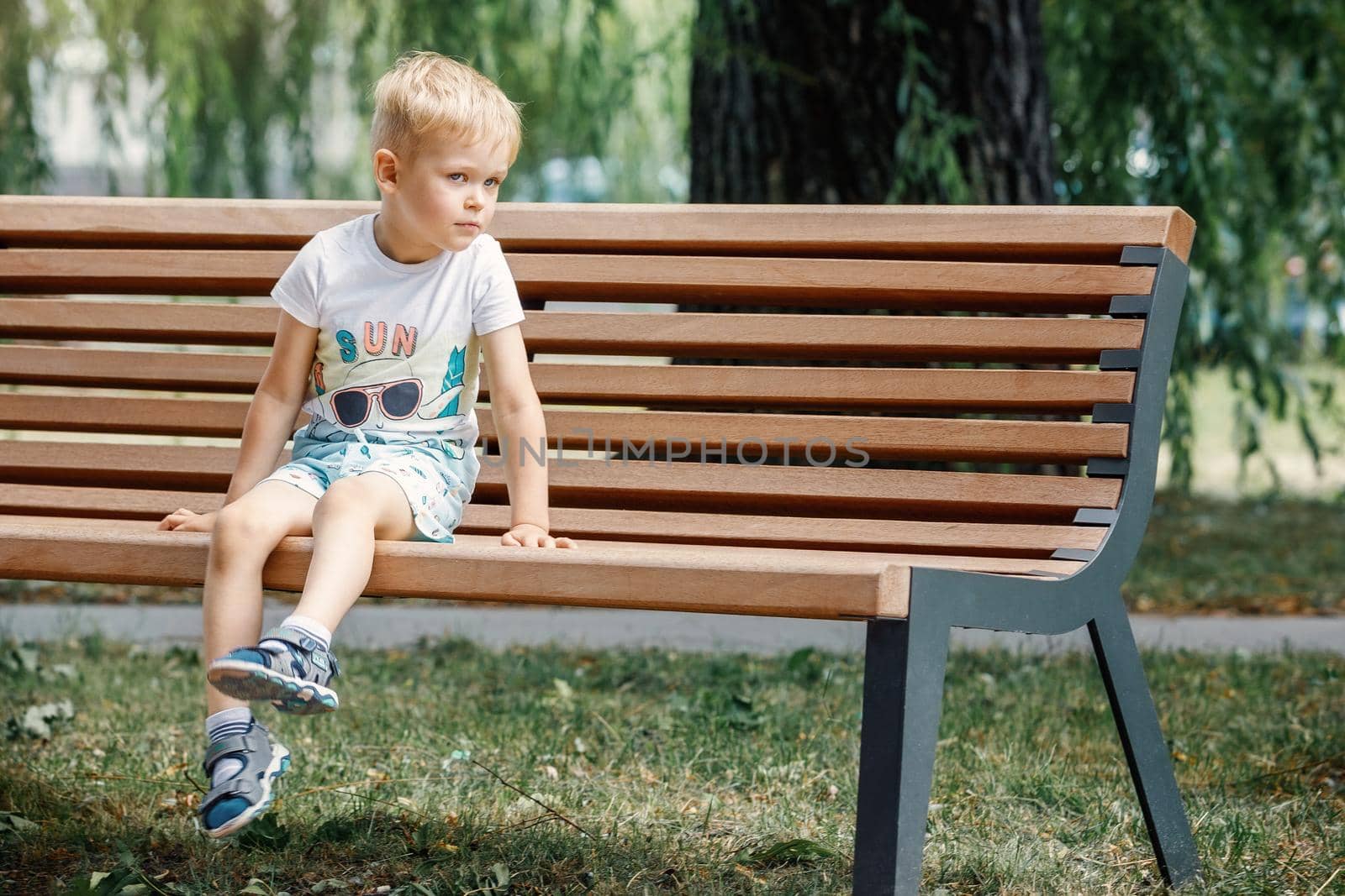 Little boy sitting on a bench. baby alone in the city. by Lincikas