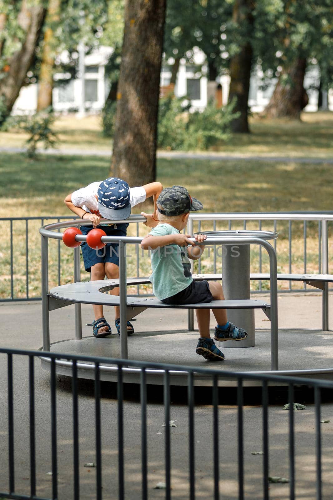 Two children on a metal children carousel spinning round.