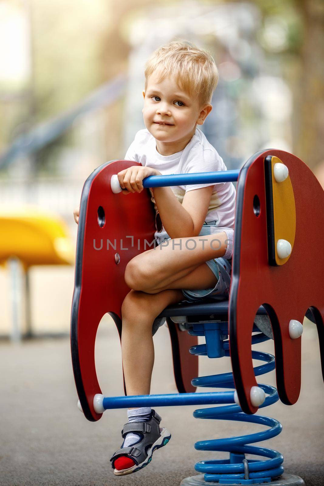 Portrait of a cute boy on a playground on a red elephant design balancing swing.