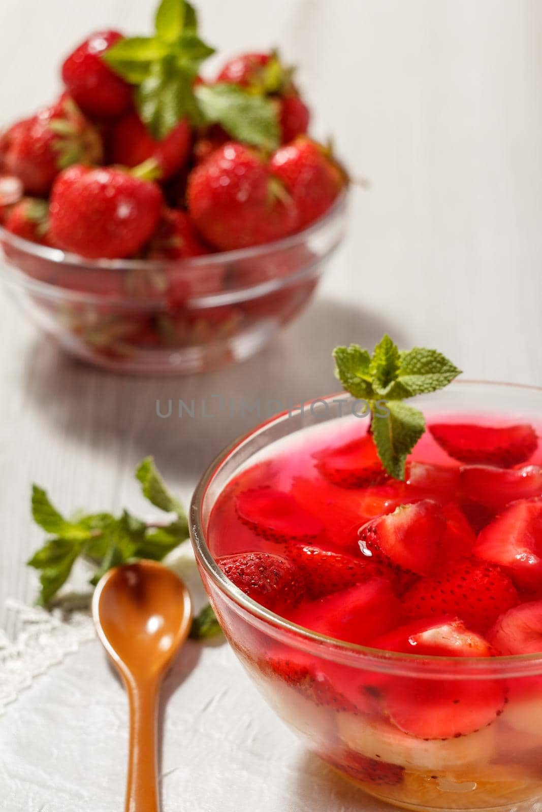 Cherry jelly with strawberry pieces in the glass bowl topped mint leaves with strawberries in a bowl on the background