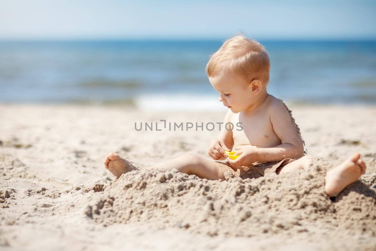 Child playing on Baltic sea beach. Little boy digging sand at sea shore. Family summer vacation. Kids play with water and sand toys. Travel with young children.