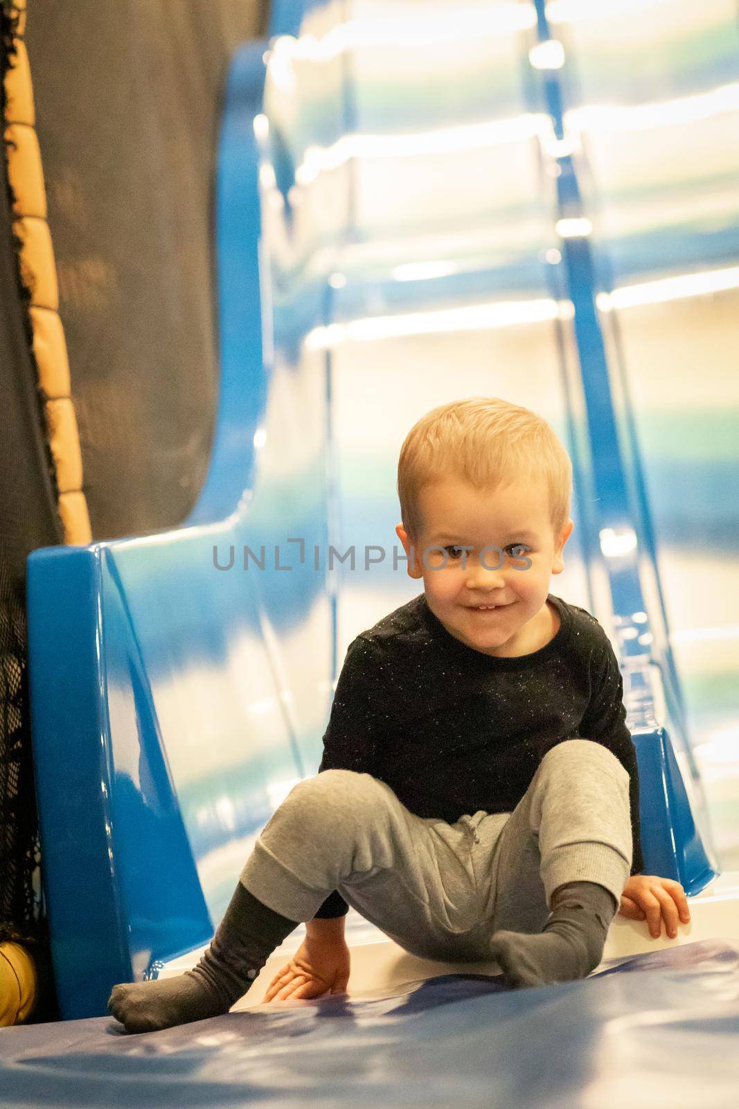 Little toddler boy sliding on shiny metal slide in amusement park at shopping mall