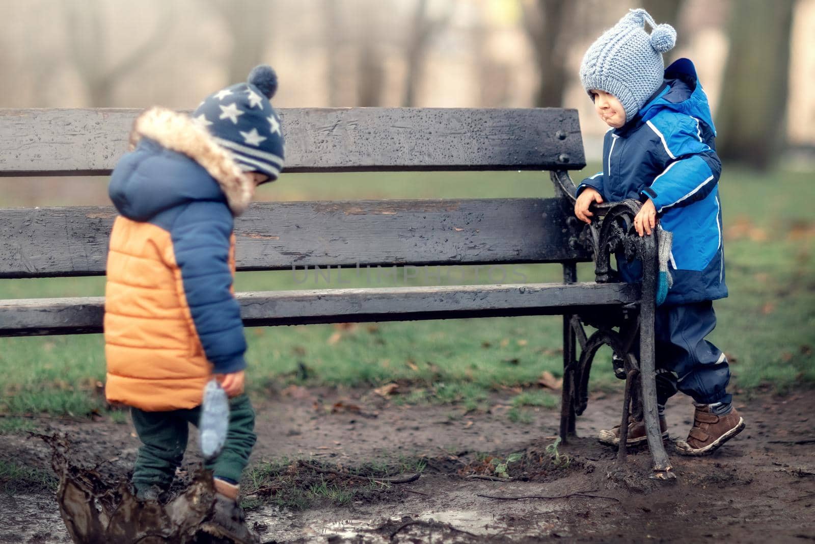 One child stands in a swamp and splash its dirt with his new shoes, his friend watches and thinks he is behaving badly.