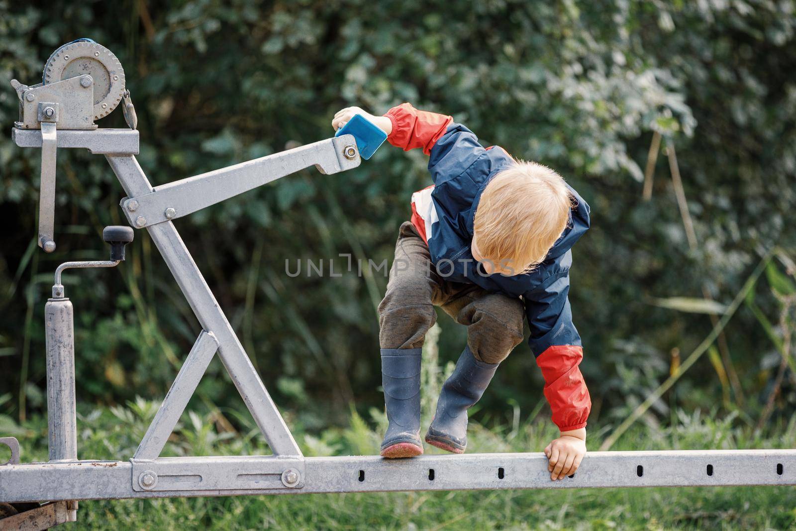 The little fisherman is playing on boat trailer winch. An agile and energetic child does not calm down in one place he enjoys climbing by Lincikas