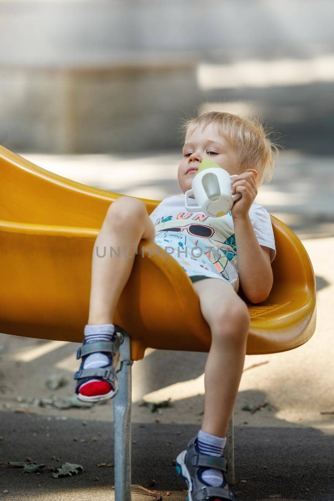 The little boy slips into a yellow plastic slide, his hair becomes eclectic, child sits down comfortably to calm and drink.