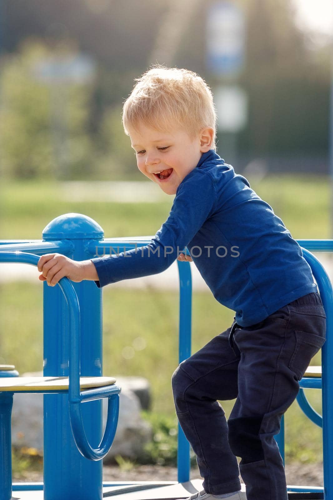 Caucasian boy spins on a children's carousel on a children's walking area in the city. The boy is happy and smiles. by Lincikas