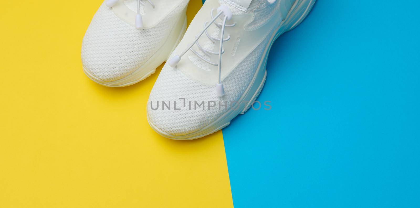 White textile sneakers on a blue yellow background, top view by ndanko