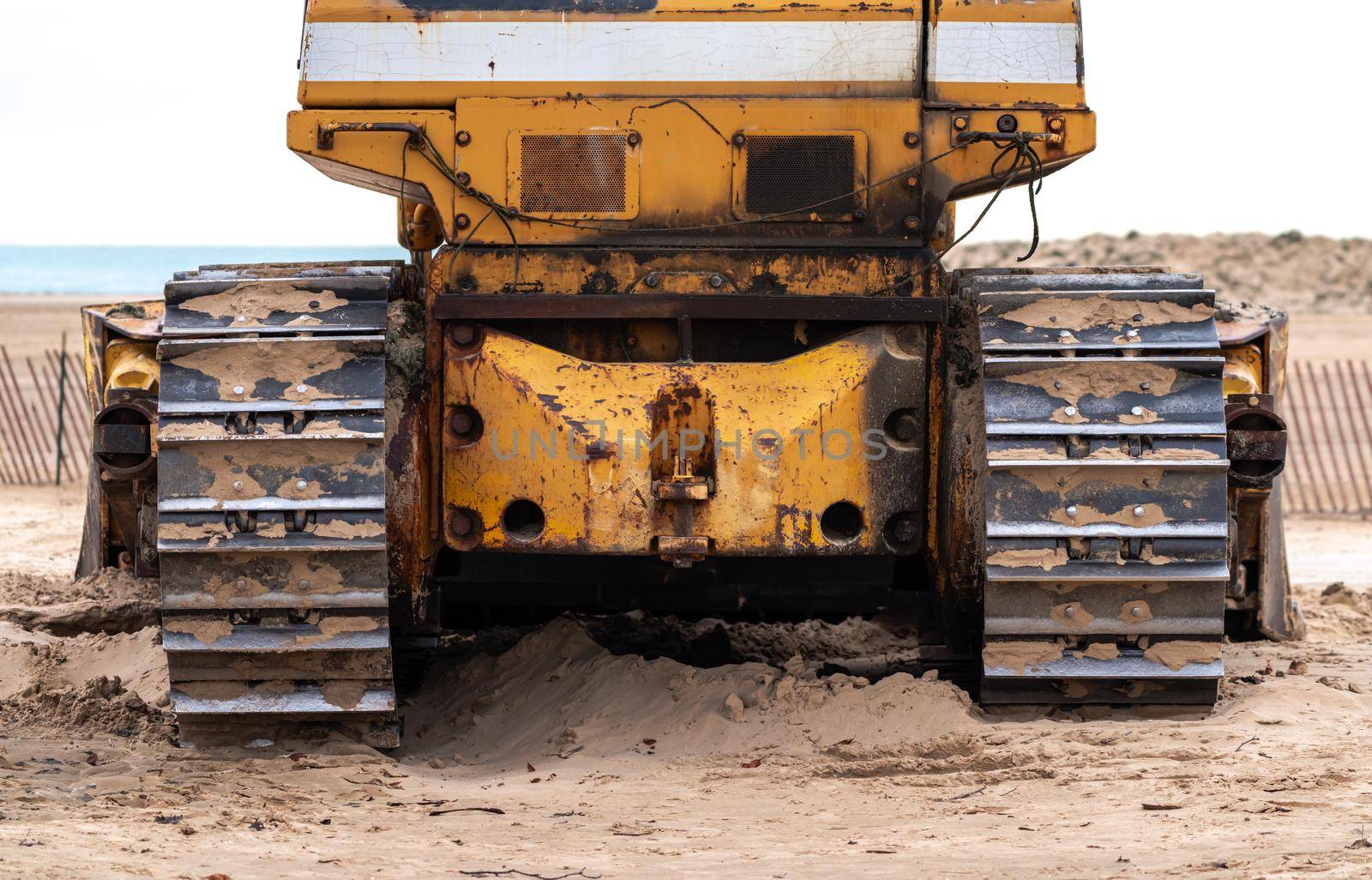 A closeup photograph of the back of an old large industrial yellow bulldozer machine weathered, worn and rusty sitting on a beach in Chicago.