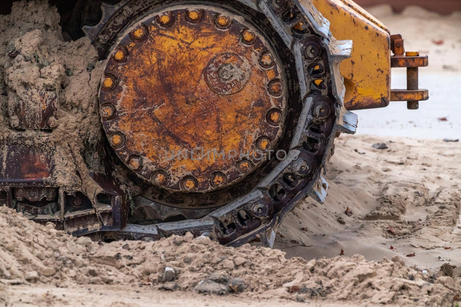 A closeup photograph of the track of an old large industrial yellow bulldozer machine weathered, rusty and worn sitting on a beach in Chicago.
