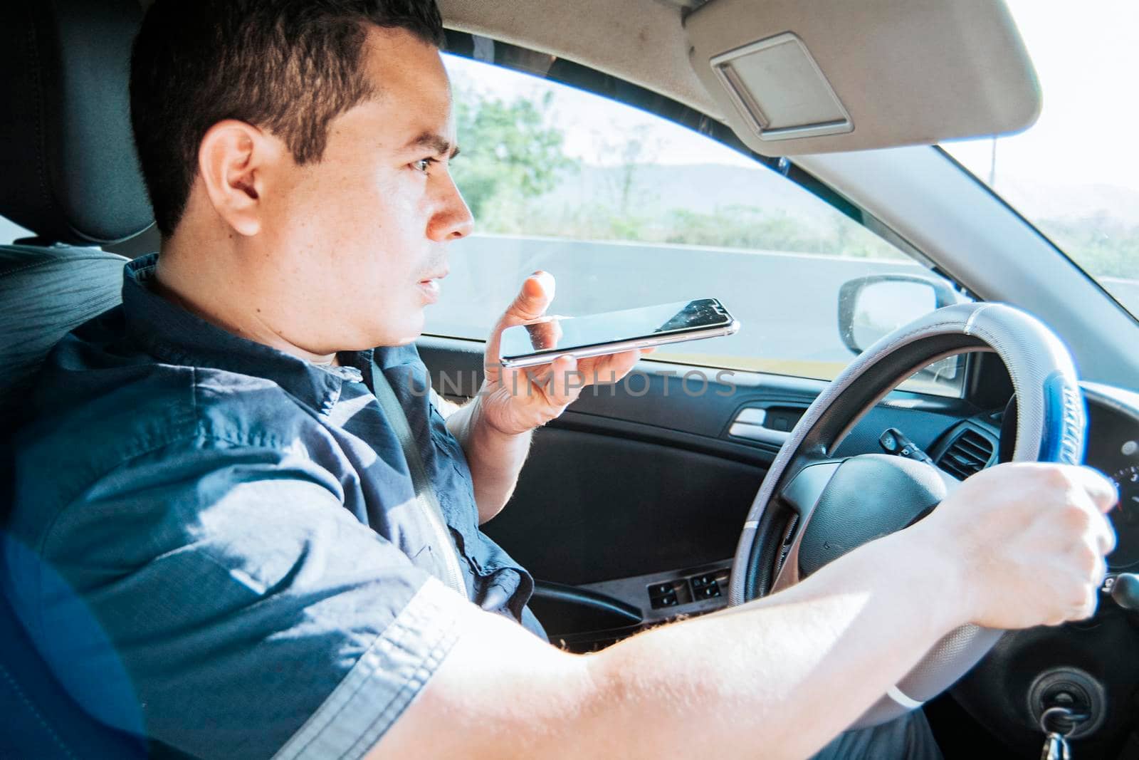 Man in his car sending voice notes with his cell phone, Side view of a young man sitting inside the car talking on the phone while driving, Young man sitting in the car talking on the phone while driving