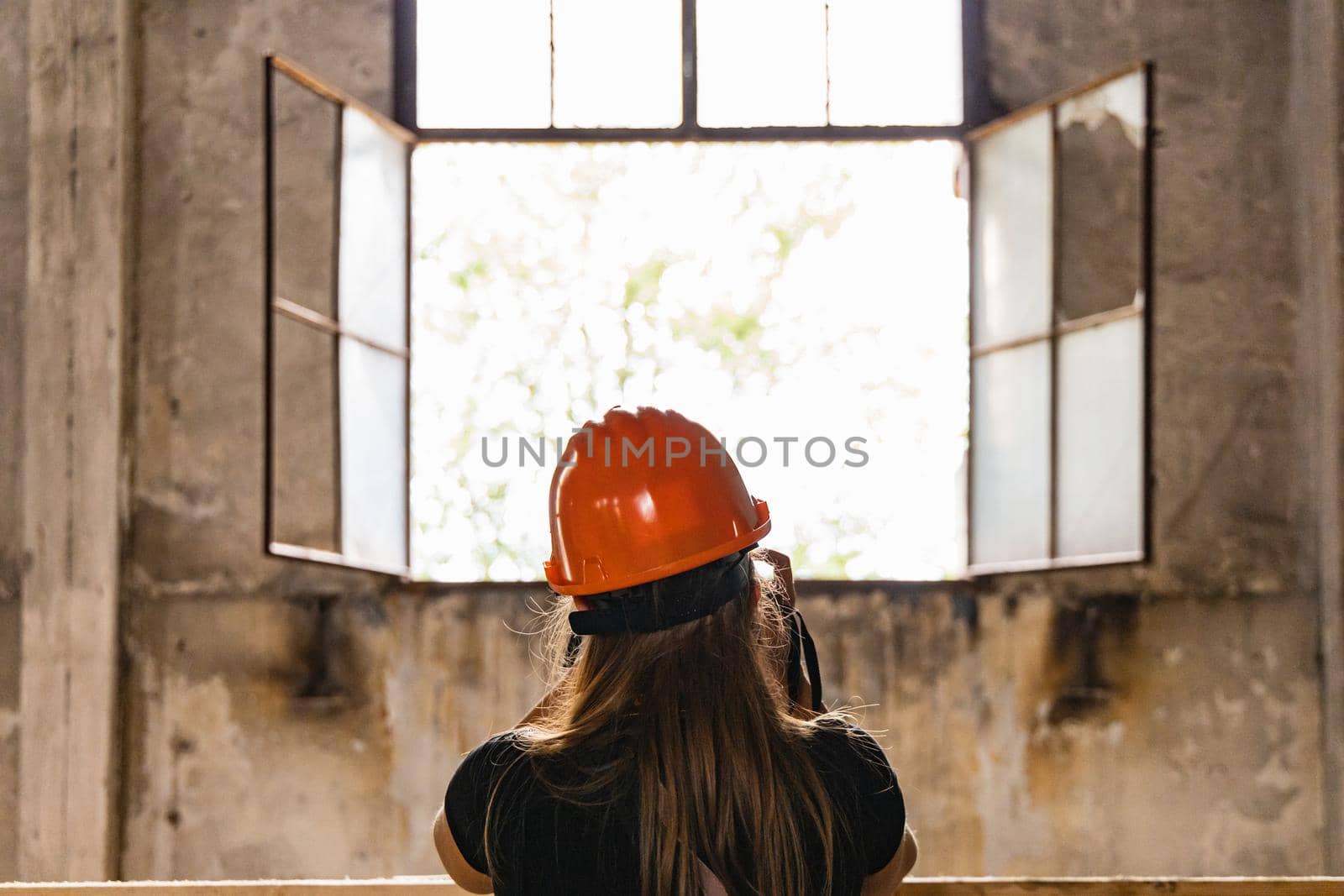 Woman in orange helmet on head standing in front of open window of old boiler building 
