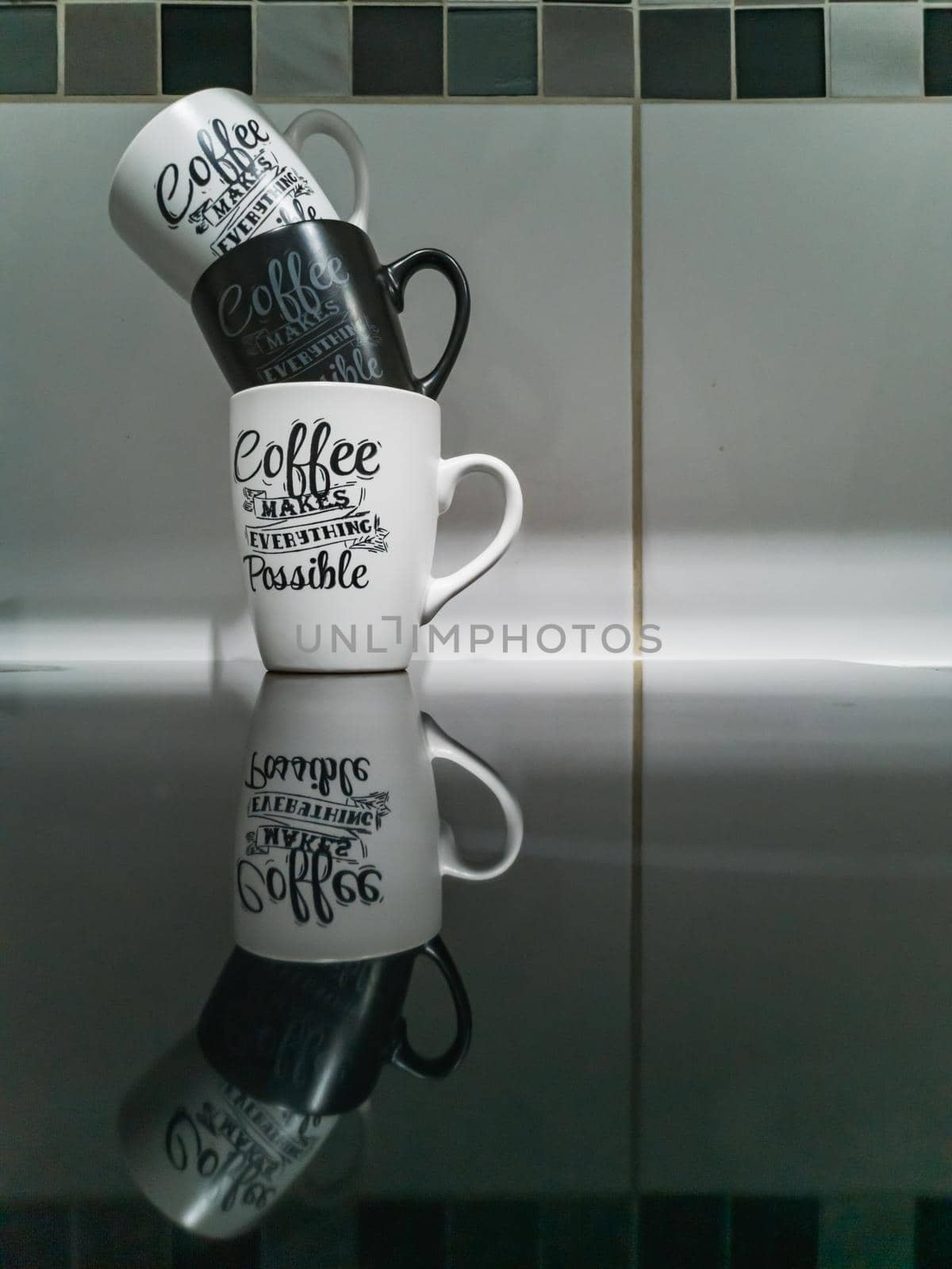 Stack of black and white mugs with calligraphy writings on it standing on reflective black surface