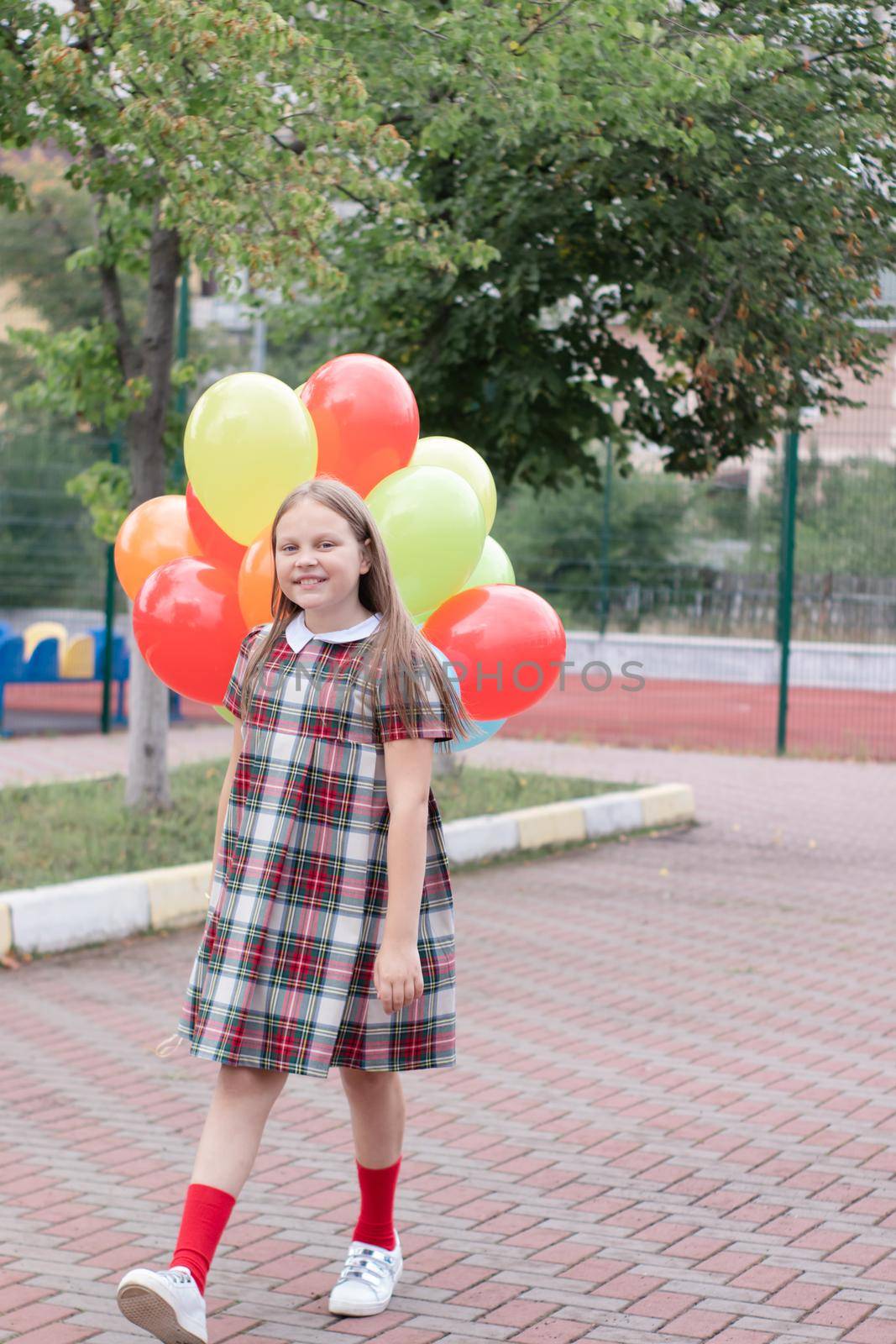 charming teenage girl in checkered brown dress with bunch of colorful balloons. school girl. pretty tween by oliavesna